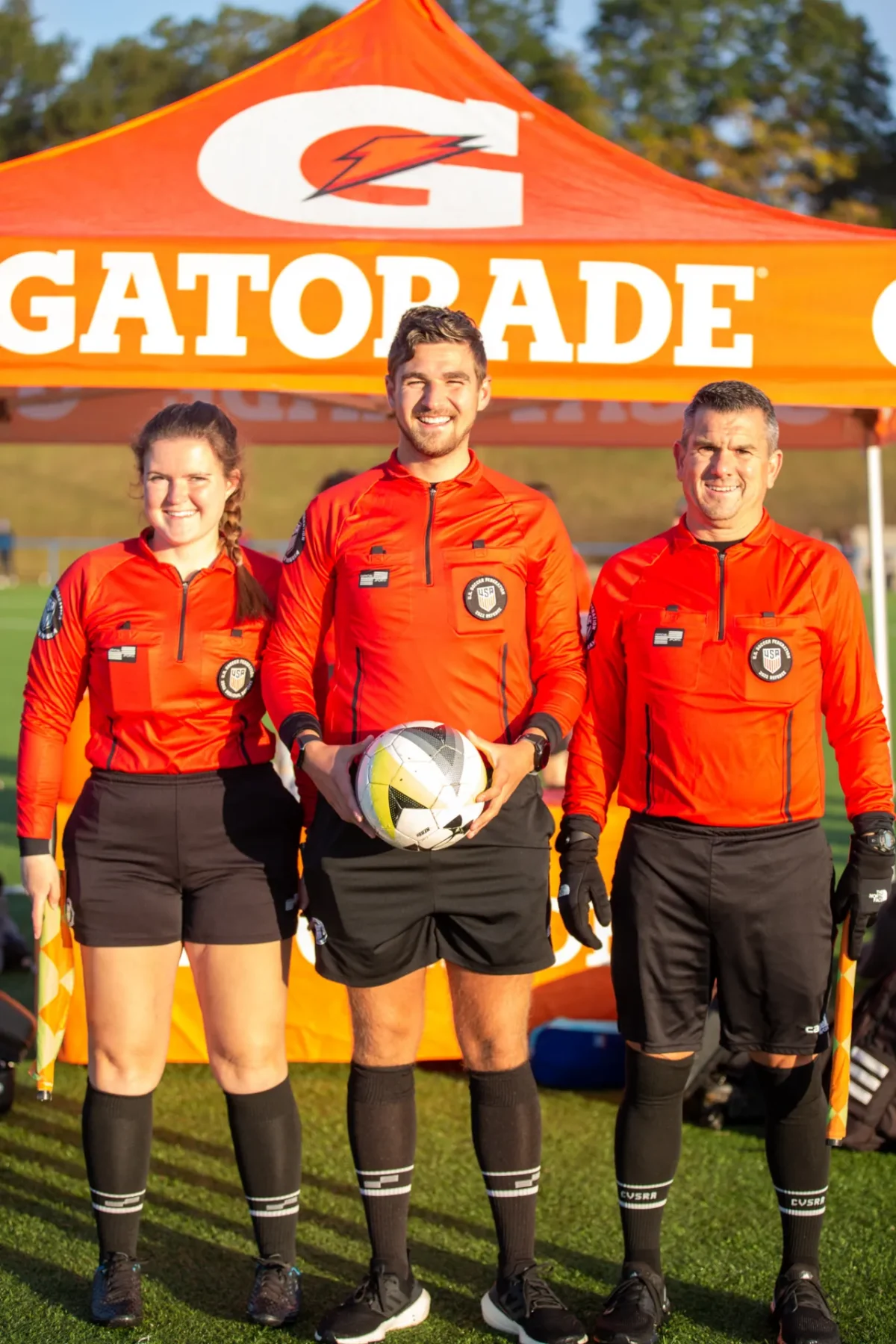 Referee crew of three posing under a Gatorade tent